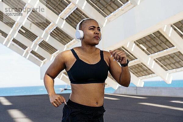 Confident sporty woman wearing headphones jogging on road