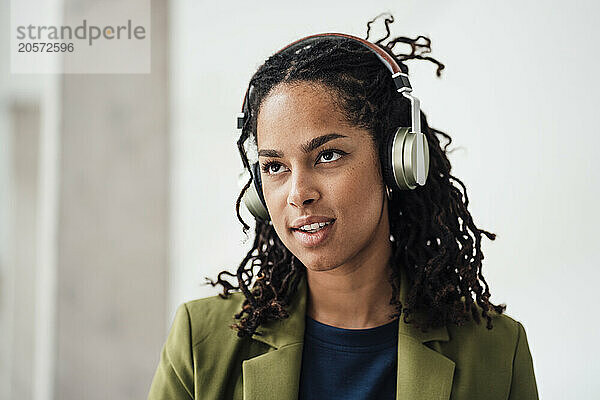 Confident young businesswoman listening to music through wireless headphones in office