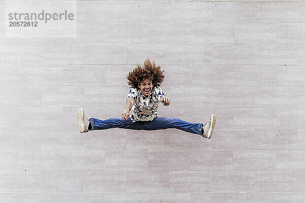 Happy man with legs apart jumping in front of wall