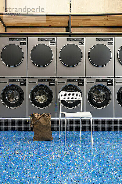 Tote bag by chair in front of washing machines and dryers at laundromat