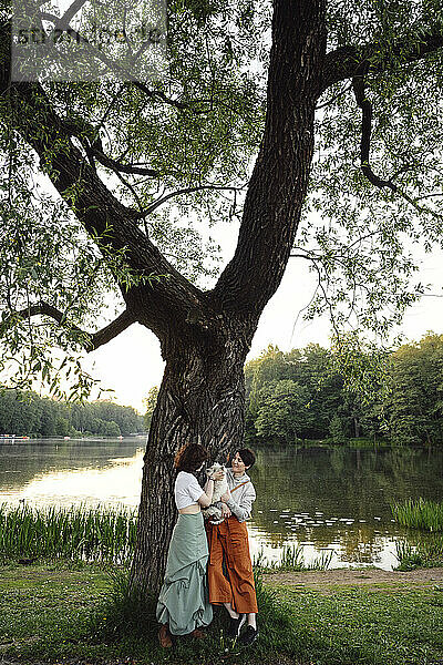 Mother and daughter with dog in front of tree near river at park