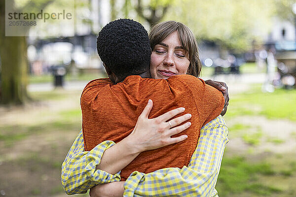 Smiling young woman with eyes closed hugging friend at park