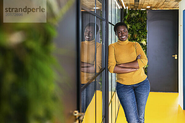 Smiling businesswoman leaning with arms crossed on wall at office