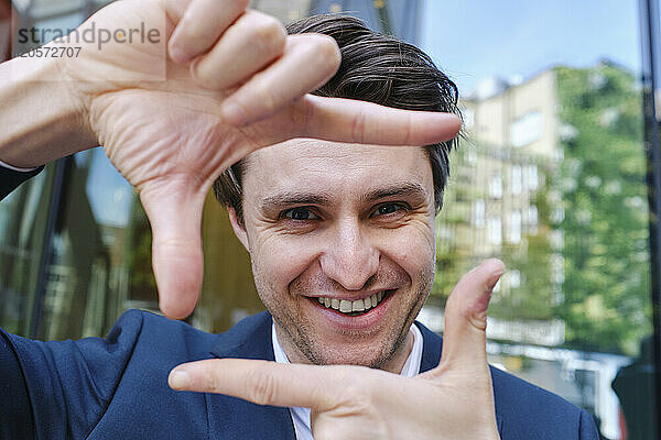 Happy businessman looking through finger frame