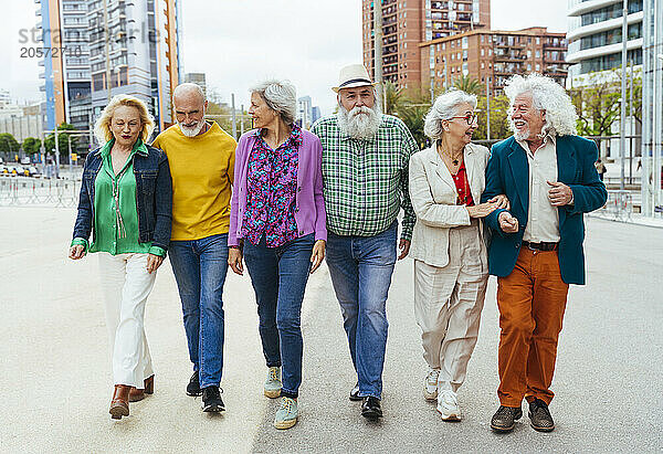 Happy senior friends walking on street in city