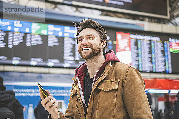 Happy man holding smart phone and looking away at airport