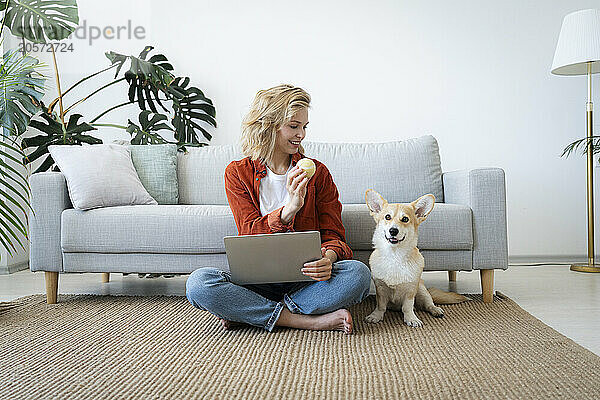 Smiling freelancer playing with pet dog sitting on carpet at home