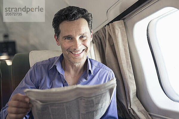 Smiling mature businessman with newspaper sitting in airplane