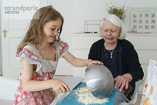 Girl pouring flour on table by grandmother at home