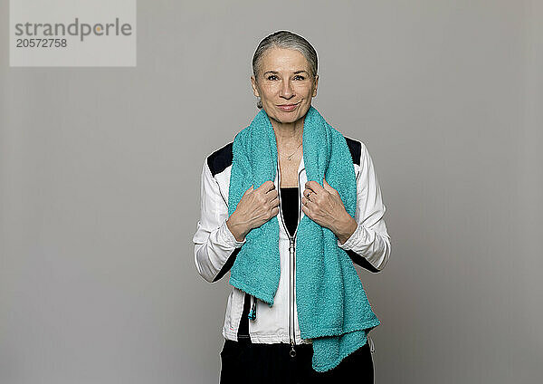 Smiling senior woman with turquoise towel standing against gray background