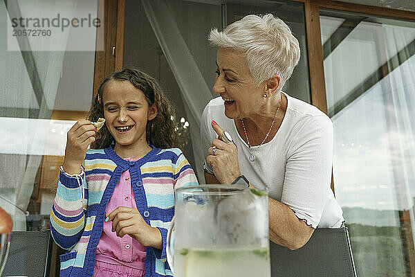 Cheerful grandmother playing with granddaughter eating snack