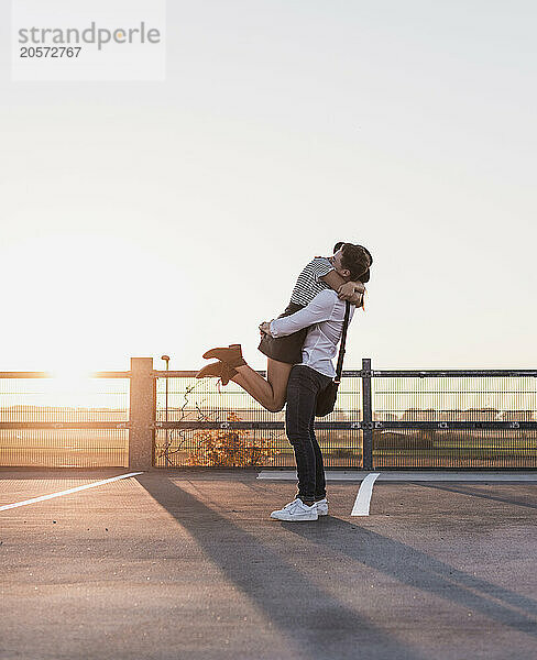 Young woman embracing girlfriend standing on road under clear sky at sunset