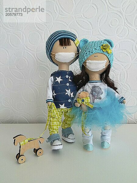 Two handmade dolls in masks  one holding a wooden dog toy  set against a white background