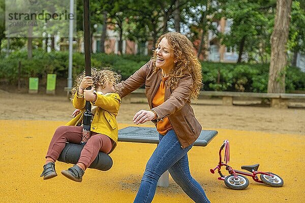 Happy scene of a caucasian adult mother playing with a girl swinging in a park