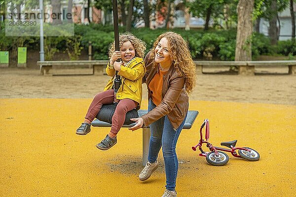 Caucasian adult mother pushing a girl on a swing in a park