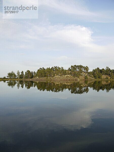 Rocks  trees and clouds are reflected in Lake Vänern  in the beautiful bay of Slöingen  atmosphere in sweden on lake vänern