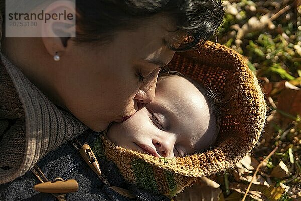 Closeup of mother kissing her son lying in park on autumn leaves