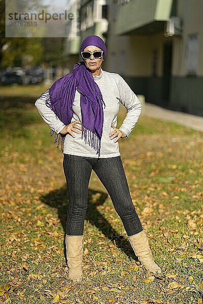 Sexy woman in her 60s wearing jeans and a bandana on her head posing sensually in the park