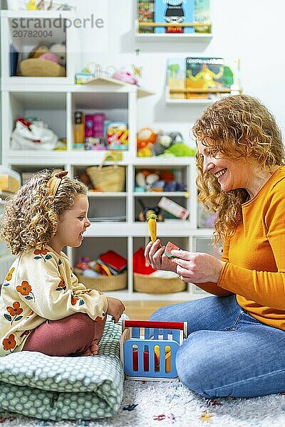 Vertical photo of a cute girl and mother playing with toys in the bedroom together