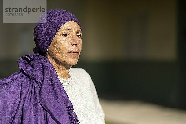 Portrait of a woman in her sixties undergoing cancer treatment with her head covered by a scarf with an expression of strength