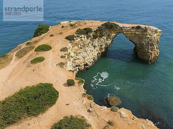 Natural rock arch by the sea  surrounded by water and some vegetation  aerial view  Arco de Albandeira  Lagoa  Algarve  Portugal  Europe