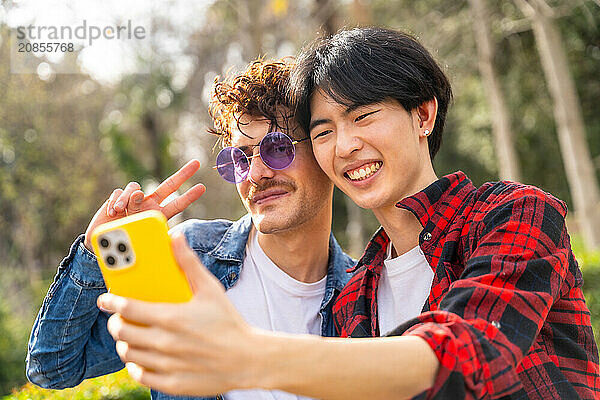 Close-up of a multiracial gay couple gesturing success while taking selfie in a park