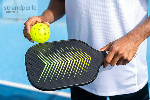 Unrecognizable close-up sportive man with pickleball equipment holding racket and yellow ball in an court