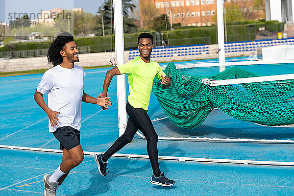 Two african american happy friends smiling while training in an outdoor running track