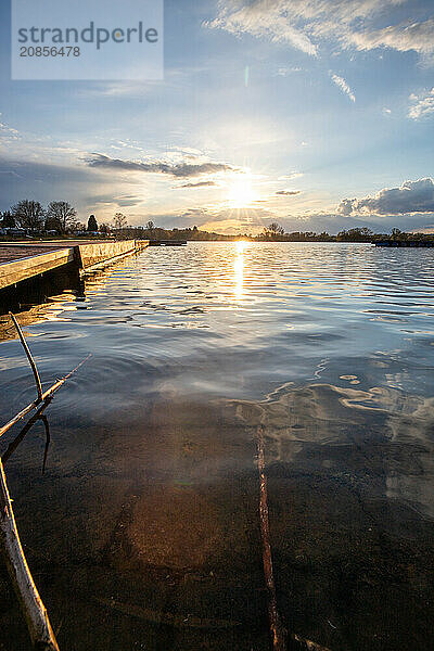 View from the shore into the distance and a sunset on the lake. The surroundings and the marvellous sky are reflected in the water. A great landscape shot Dutenhofener See  Hesse Germany