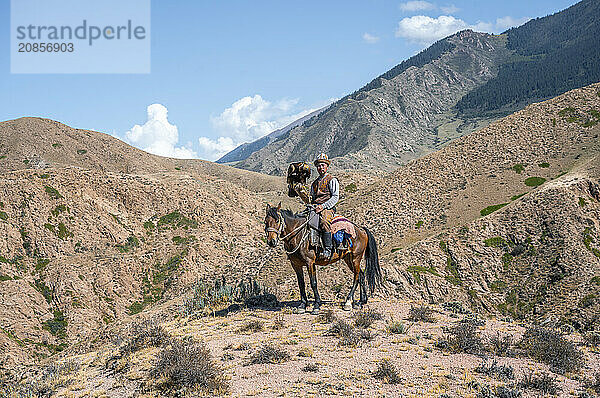 Traditional Kyrgyz eagle hunter riding with eagle in the mountains  hunting on horseback  near Bokonbayevo  Issyk Kul region  Kyrgyzstan  Asia