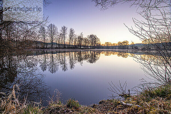 View from the shore into the distance and a sunset on the lake. The surroundings and the marvellous sky are reflected in the water. A great landscape shot Dutenhofener See  Hesse Germany