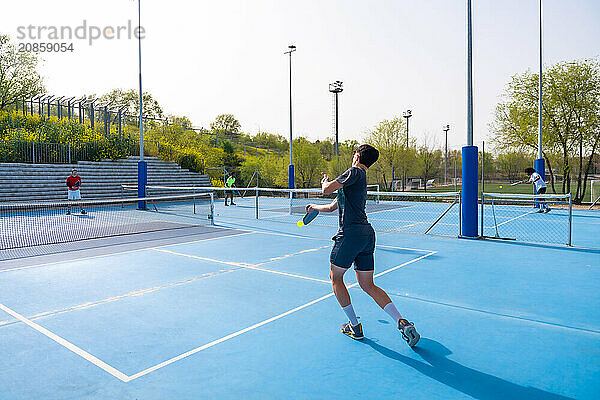 Full length of men playing pickleball in an outdoor court