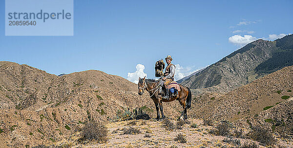 Traditional Kyrgyz eagle hunter riding with eagle in the mountains  hunting on horseback  near Bokonbayevo  Issyk Kul region  Kyrgyzstan  Asia