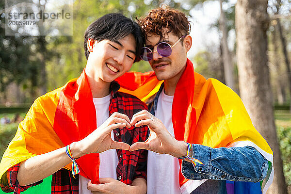 Multi-ethnic gay couple joining hands to form heart shape standing in a park