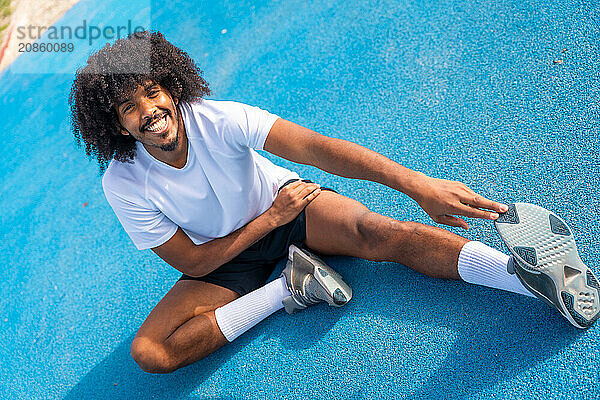 Sportive man with afro hairstyle warming up and stretching in an outdoor running track