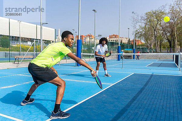 Side view full length photo of two african american young male friends having fun during pickleball match outdoors