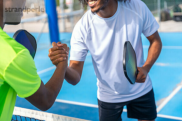 Pickleball african american male rivals shaking hands before playing a match in an outdoor court