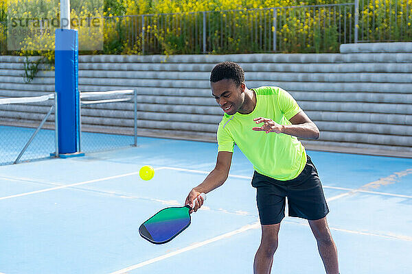 Horizontal photo with copy space of an african young man playing pickleball in an outdoor court