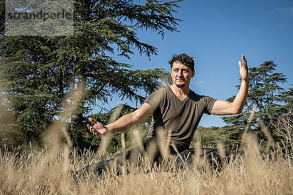 A middle-aged Caucasian man practices Kung Fu on a hill  performing stretching  balancing  and strength exercises