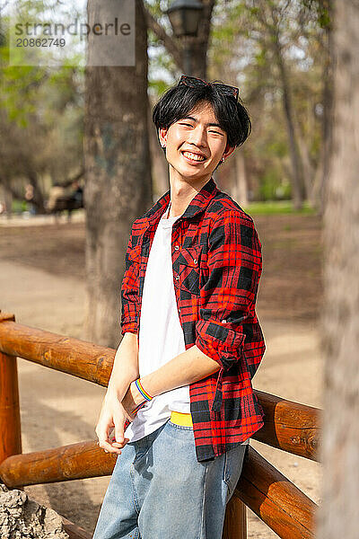 Vertical portrait of an asian gay man standing in a park smiling at camera