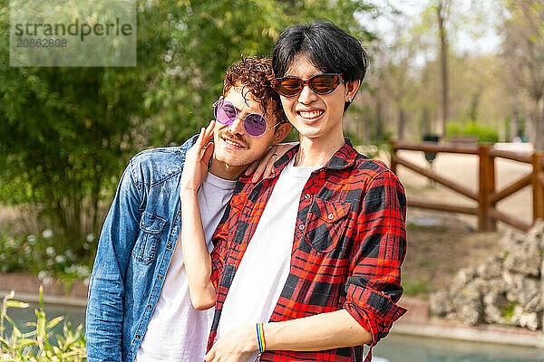 Portrait of a multi-ethnic gay couple smiling at camera standing together in a park