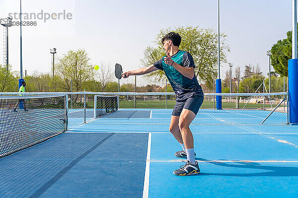 Side view of a young fit man playing pickleball in an outdoor court