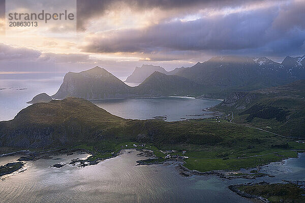 Landscape on the Lofoten Islands. View from the mountain Offersoykammen to the sea  the mountains Veggen  Mannen  Himmeltindan and Hogskolmen as well as the beaches of Haukland (Hauklandstranda) and Vik (Vik Beach) . At night at the time of the midnight sun. Clouds in the sky  sunlight from the side. Vestvagoya  Lofoten  Norway  Europe