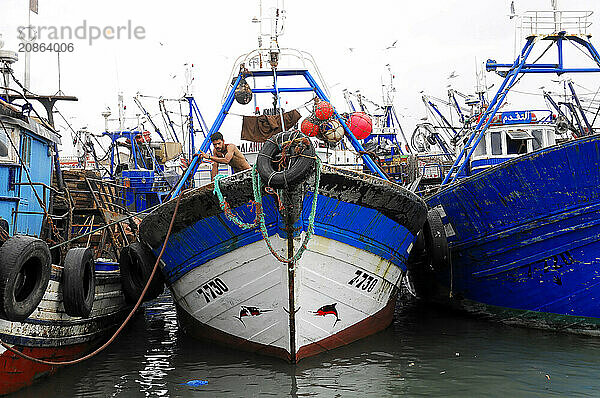 Essaouira  A fisherman works on board a boat in the harbour  surrounded by other colourful boats  Essaouira  Morocco  Africa