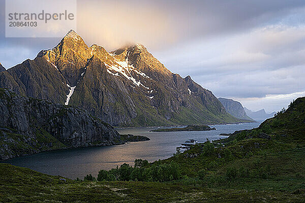 Mountain landscape in the Lofoten Islands. View across the Maervollspollen fjord to mountains in the night sunlight. At night at the time of the midnight sun  clouds and sun. Mountain peaks in the sunlight. Early summer. Vestvagoya  Lofoten  Norway  Europe