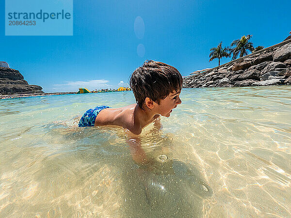 A young boy is swimming in the ocean. The water is clear and calm. The boy is wearing a blue swimsuit