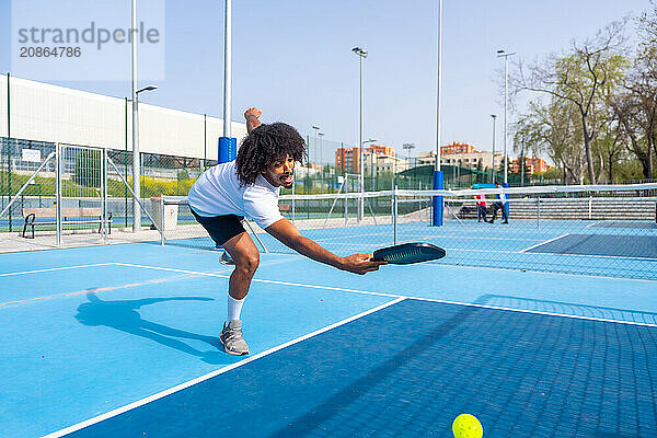 Full length photo of an african sportive man trying to reach the ball playing pickleball in an outdoor court