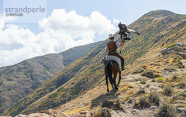 Traditional Kyrgyz eagle hunter riding with eagle in the mountains  hunting on horseback  near Bokonbayevo  Issyk Kul region  Kyrgyzstan  Asia