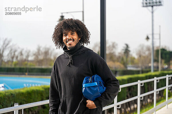 African man going to play pickleball carrying bag with racquet next to the court