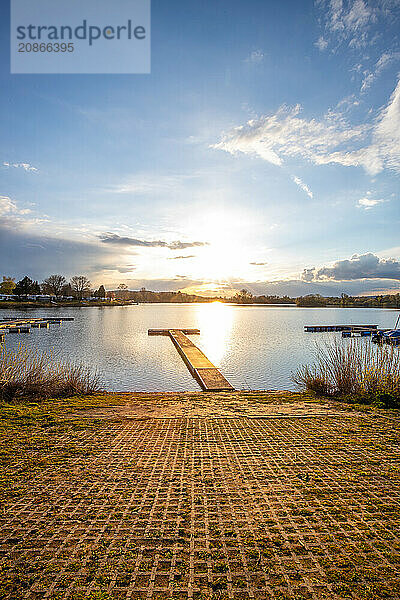 View from the shore into the distance and a sunset on the lake. The surroundings and the marvellous sky are reflected in the water. A great landscape shot Dutenhofener See  Hesse Germany